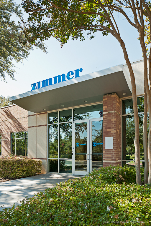 Exterior entrance of the Zimmer Biologics facility featuring the company sign, brick columns, and glass facade