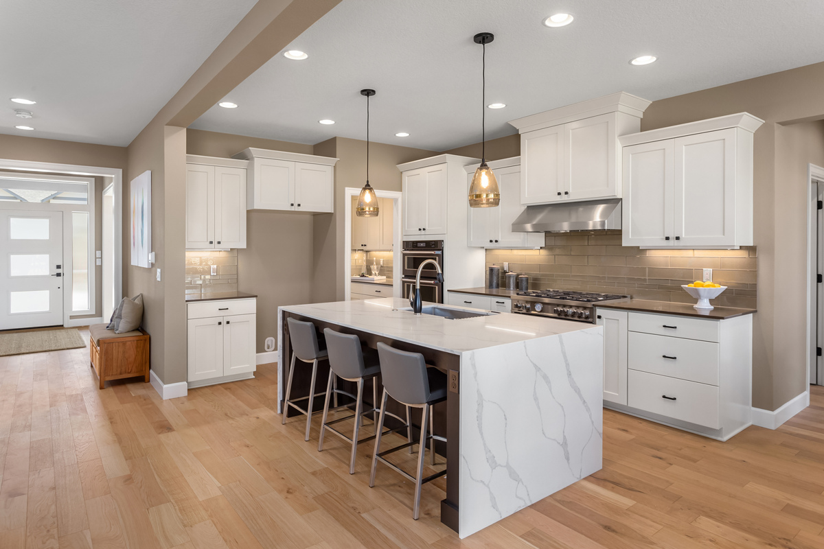 Remodeled kitchen with white shaker cabinetry, marble waterfall island, pendant lighting, and hardwood floors in an Austin home