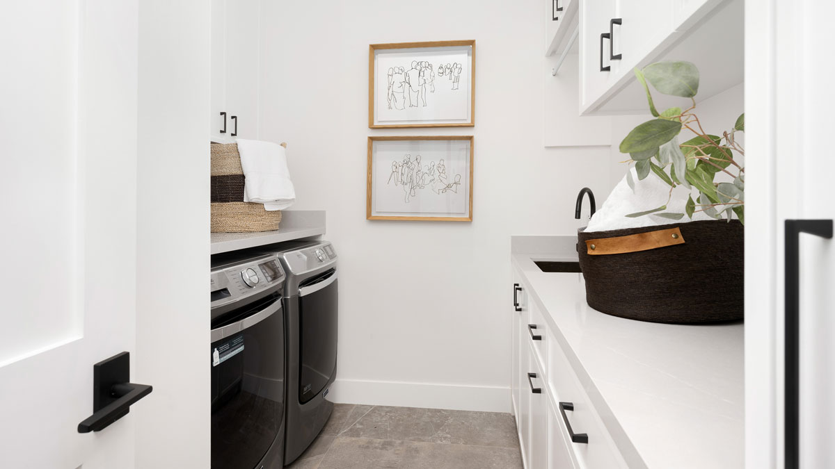 Bright laundry room with stacked washer and dryer, white cabinetry, open shelving, and a woven basket with a potted plant