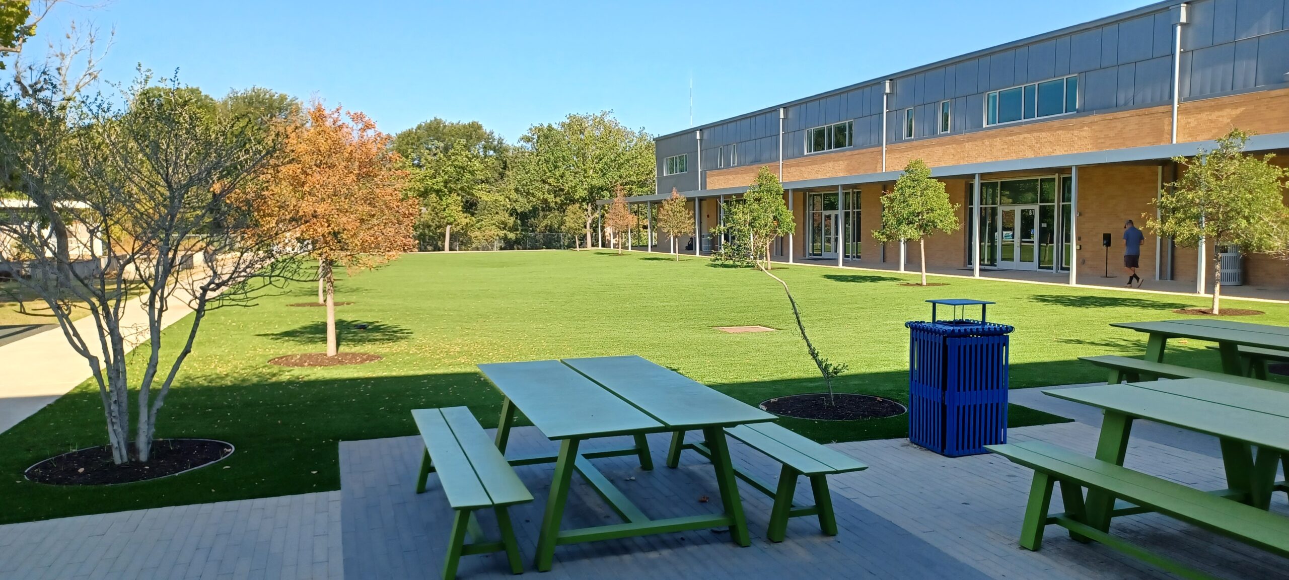Outdoor patio and artificial turf at Casis Elementary School with green picnic tables, planters, and the school building in the background