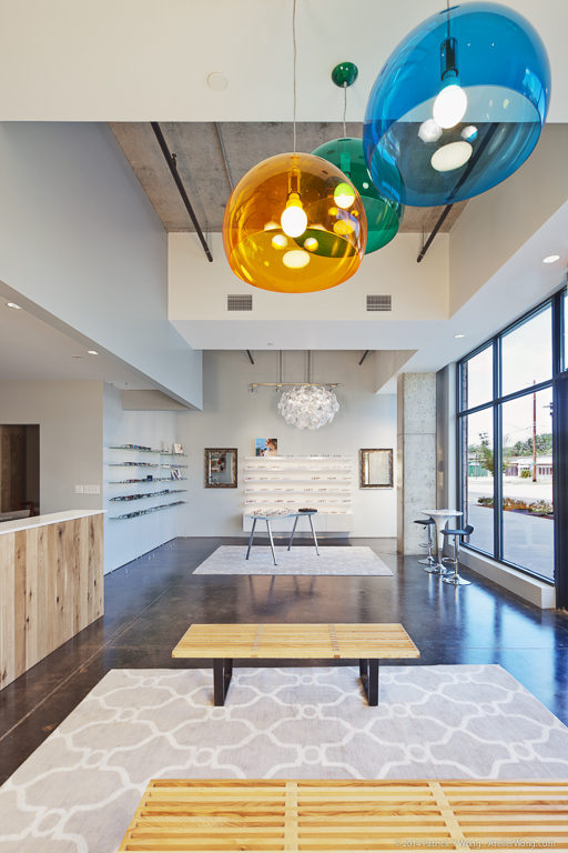 Open retail floor of EyeRis Vision featuring eyewear display shelving, a gold pendant light, and floor-to-ceiling windows