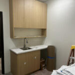 Tenant improvement in progress with a new break area, light wood upper and lower cabinets, white countertop, and undermount sink