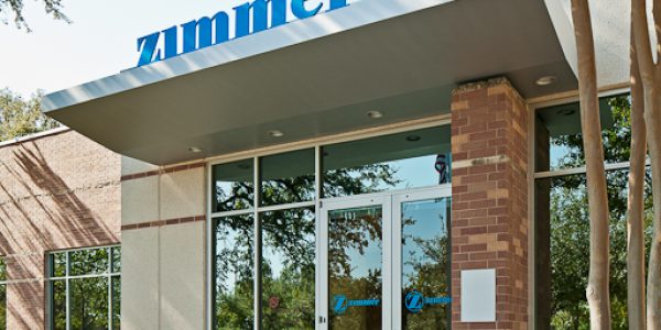 Exterior entrance of the Zimmer Biologics facility featuring the company sign, brick columns, and glass facade