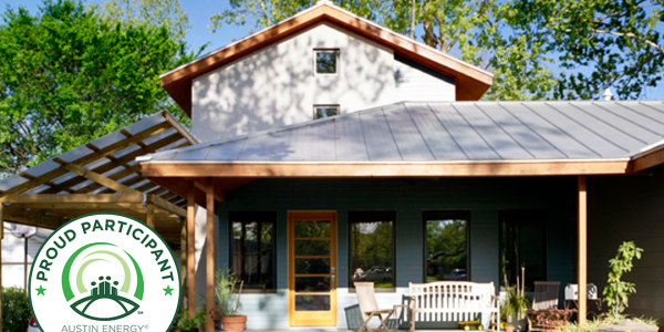 Renovated home exterior with dark green siding, metal roof, wood-trimmed gable, and covered porch; Austin Energy Green Building "Proud Participant" badge in corner.