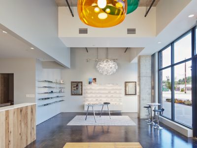 Open retail floor of EyeRis Vision featuring eyewear display shelving, a gold pendant light, and floor-to-ceiling windows