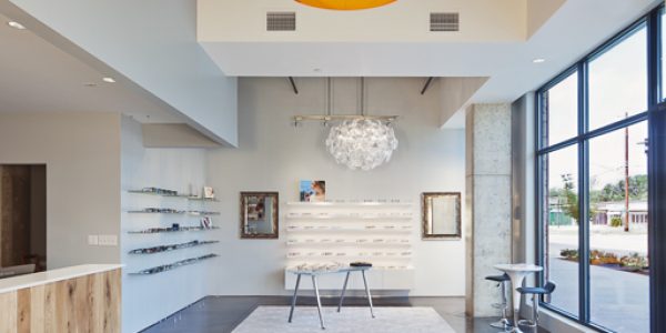 Open retail floor of EyeRis Vision featuring eyewear display shelving, a gold pendant light, and floor-to-ceiling windows