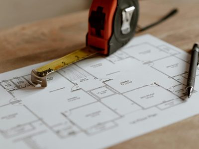 Architectural floor plan spread flat with a tape measure and pen resting on top, viewed from above.