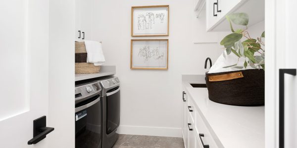 Bright laundry room with stacked washer and dryer, white cabinetry, open shelving, and a woven basket with a potted plant