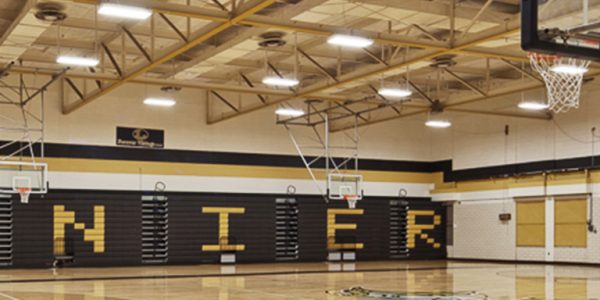 Interior of a school gymnasium at an Austin Independent School District facility, showing the hardwood court, bleachers, and overhead lighting