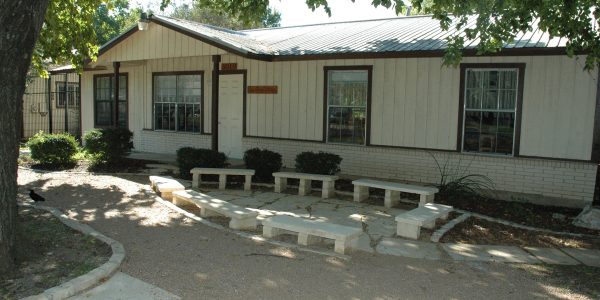 Exterior of renovated school building with stone benches and landscaped courtyard, Austin Montessori School campus expansion, Austin TX